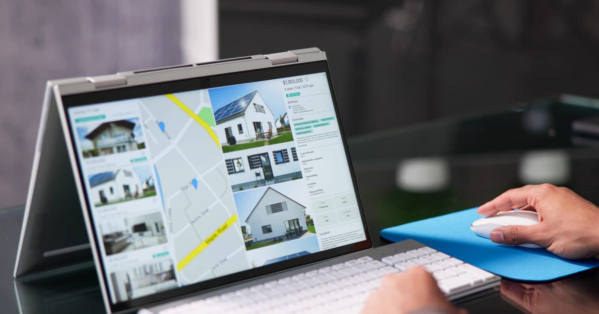 Property search results and a map displayed on a laptop while a person navigates listings