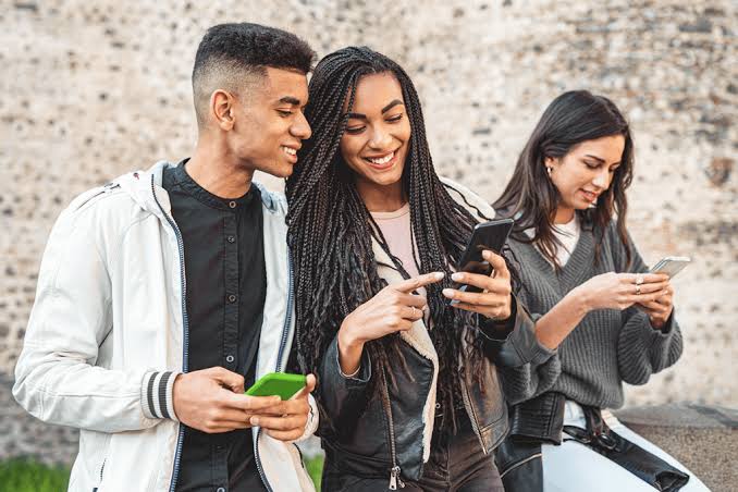 Group of young adults using mobile phones together outdoors